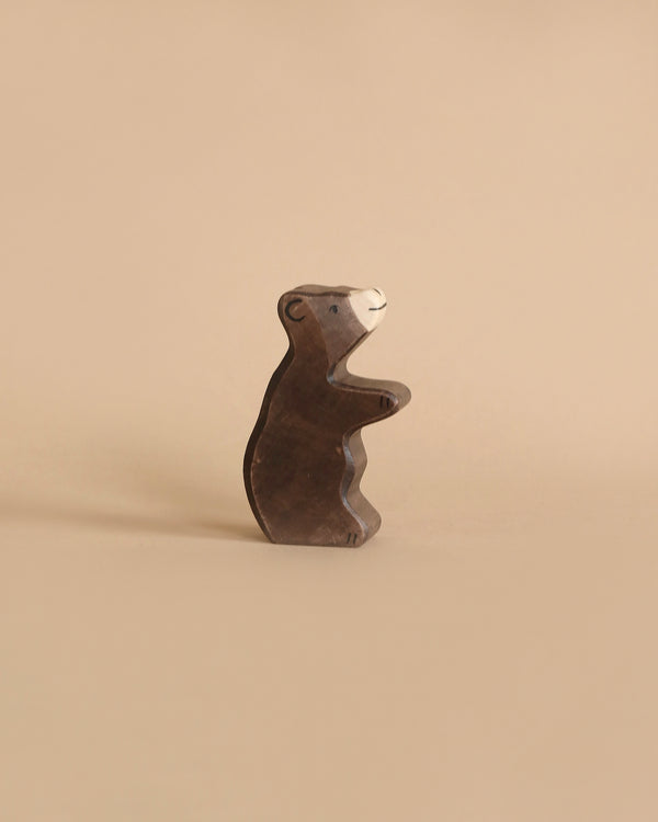 A Holztiger Little Brown Bear with a dark brown body and a light brown snout stands against a plain beige background. Made in Europe by HOLZTIGER figures, the bear is depicted in a standing position with its front paws slightly raised.