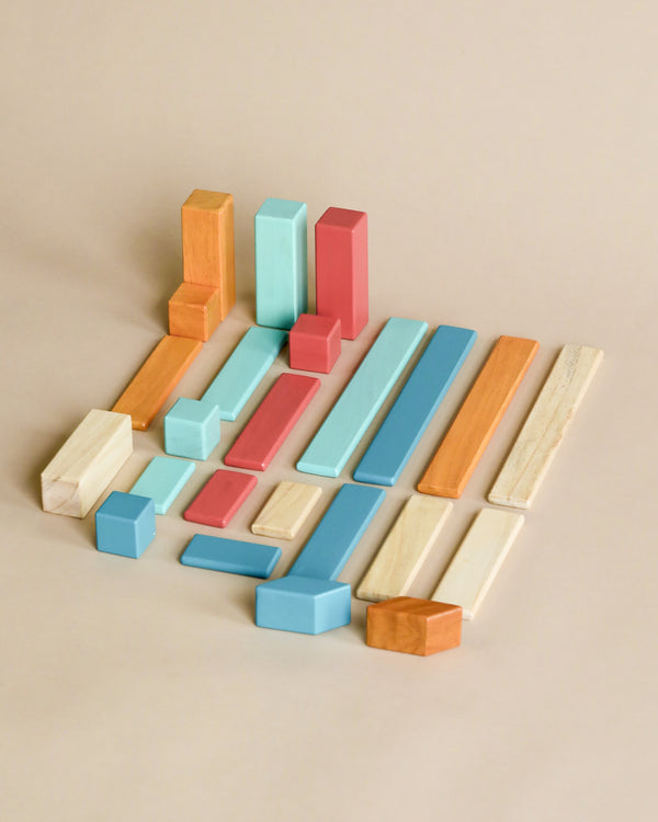 An assortment of colorful Tegu 24 Piece Magnetic Wooden Block Set - Sunset blocks, including rectangles and squares, arranged in a scattered layout on a beige background.