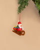 The Christian Ulbricht Ornament features Santa Claus, crafted in Germany, wearing a red outfit while riding a wooden sled and holding a gift. It hangs from a green branch set against a beige background.