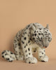 The beige backdrop showcases a Sitting Snow Leopard Stuffed Animal, featuring realistic details with gray and white fur and black spots.