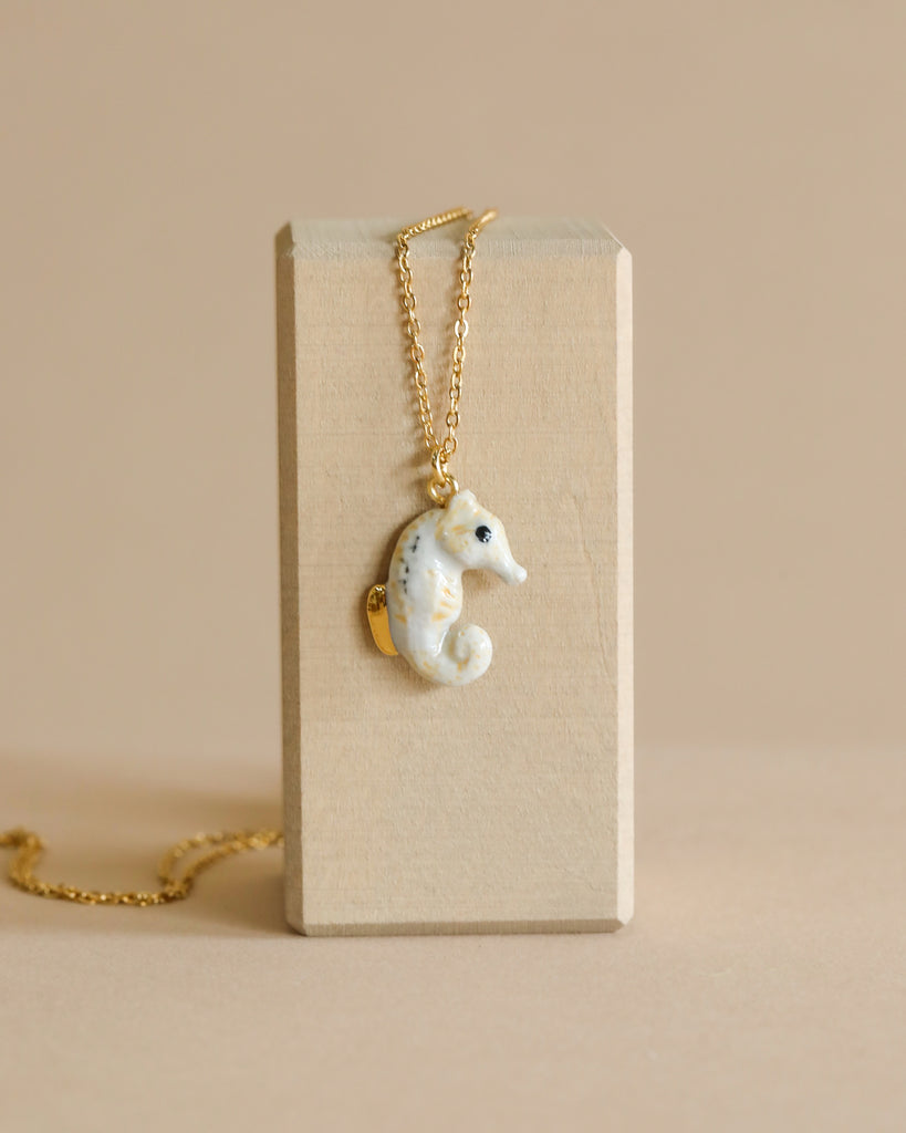 An Arctic Seahorse Necklace, displayed against a beige rectangular block on a light tan background.