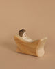 A small Ostheimer Nativity Scene figure, featuring a painted face, reclines on a wooden block against a beige background, highlighting the charm of handcrafted wooden toys. The block, made from sustainable materials, showcases a smooth, curved shape akin to a lounge chair.