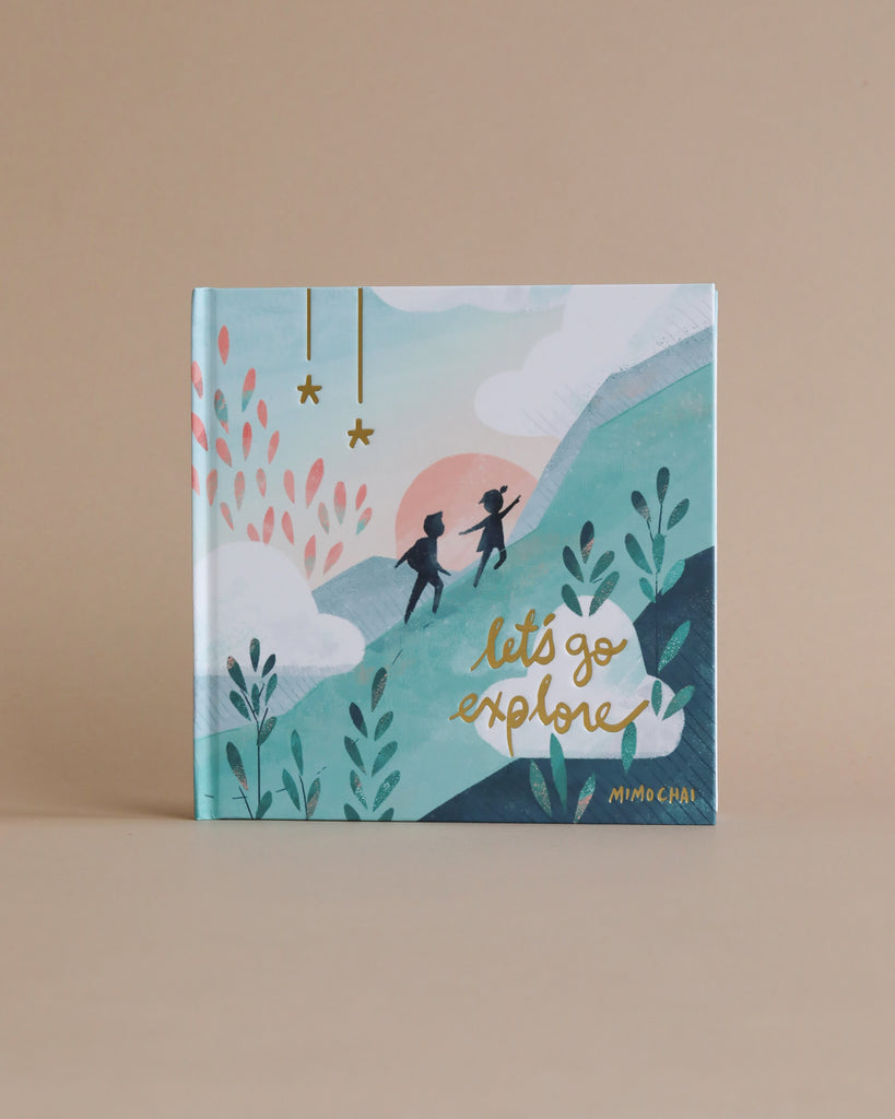 Sentence with product name: The Let's Go Explore Book by Mimi Chao, features an illustrated landscape with hills, plants, and two explorers walking under a pink sunset sky.