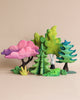 A colorful display of stylized trees in various shapes and hues, including pink, Extra Large Wooden Green Spruce Tree, and blue, painted with non-toxic paint, arranged artistically against a beige background.