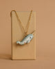 A gold chain necklace displayed on a wooden stand features the Narwhal Necklace with a white tusk and black eyes against a plain beige background.