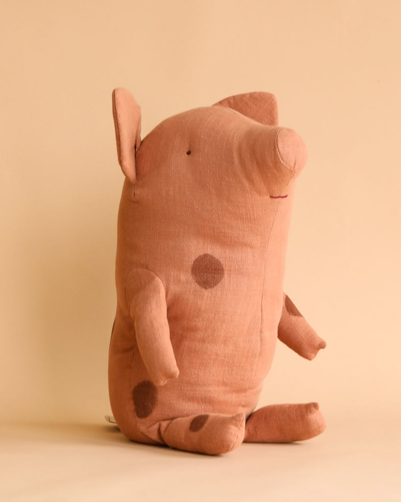 A stuffed toy resembling a large truffle pig stands upright against a plain beige background. Named the Maileg Large Truffle Pig - Vintage Rose, it is crafted from a cotton blend and features darker spots, small ears, and a simple stitched facial expression. Its minimalist design is complemented by its soft handfeel.