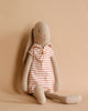 The Maileg Bunny Size 4, dressed in a red and white striped sailor outfit, sits against a beige background, ready for adventure.