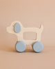 A Wooden Puppy Push Toy, featuring two light blue wheels and a light blue ear, is set against a beige background. With its minimalist design and no other markings, this charming toy helps develop fine motor skills.