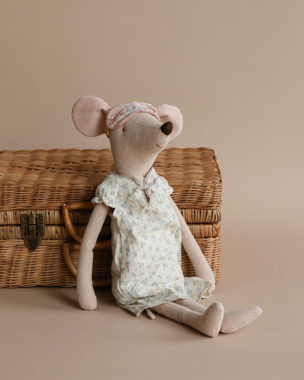 Maileg Maxi Mouse in Nightgown, a plush doll in a floral nightgown and headband with a bow, sits in front of a wicker basket with brass latches, against a beige background.