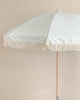 A beige Beach Umbrella with a white paisley pattern and fringe details, positioned upright against a neutral-toned background.