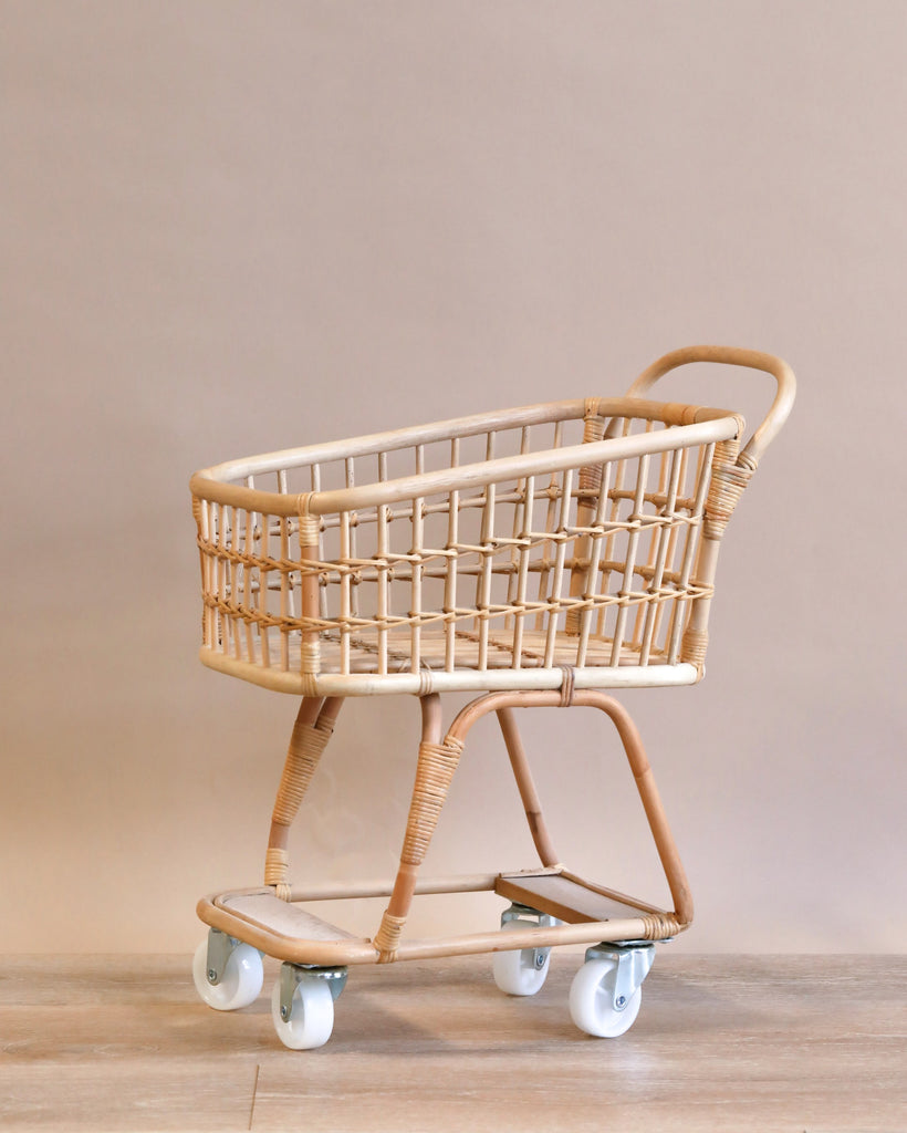 A vintage Rattan Grocery shopping cart with a metal frame and white wheels, standing against a neutral beige background.