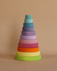 A neatly stacked pyramid of colorful wooden rings arranged by size from largest to smallest, with the largest ring at the bottom in green and the smallest at the top in light blue, all set against a plain beige background. This Pastel Stacking Tower enhances fine motor skills and eye-hand coordination.