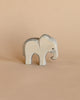 A small Ostheimer elephant figurine stands on a beige background. This handcrafted wooden toy has a simple, smooth design with visible wood grain and a small, painted eye.