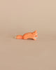 A small, handcrafted Ostheimer Small Fox - Creeping figurine lies on a plain beige background, depicted in a sleek and minimalist design with smooth contours and a subtle orange hue.