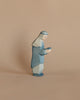 A small, handcrafted wooden figurine, known as the Ostheimer Blue King, features a character adorned in a blue robe with a head covering, holding a small object in their hands. The background is a plain, light brown surface, making it perfect for imaginative play with other Ostheimer toys.