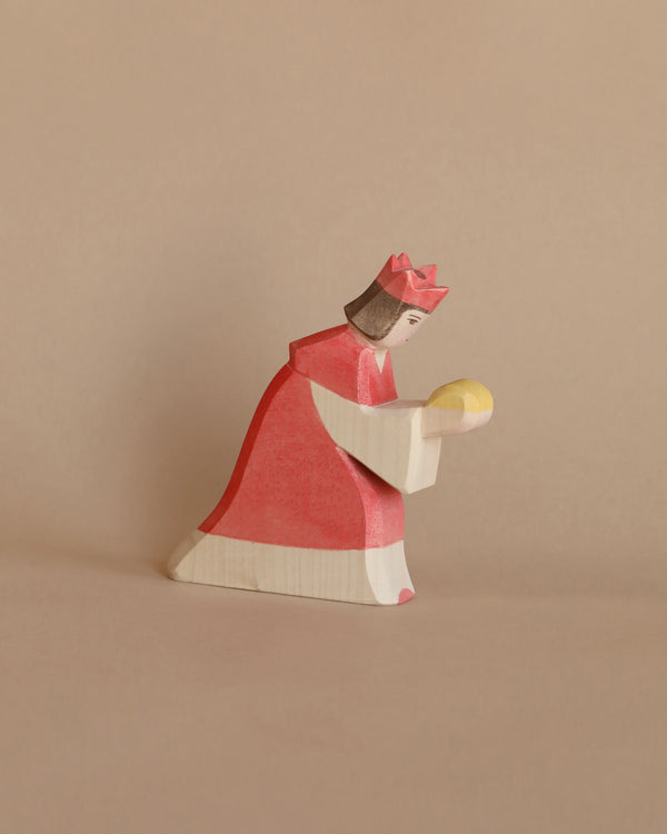 A handcrafted Ostheimer Red King With Crown, holding a golden orb, set against a plain beige background. The figure is stylized with simple, smooth shapes and muted tones.