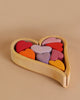 A Grimm's Red Hearts Building Blocks filled with vibrant heart-shaped building blocks in various shades, including red, pink, purple, orange, and yellow. Perfect for enhancing fine motor skills, this charming desk-toy adds a splash of color to any beige background.