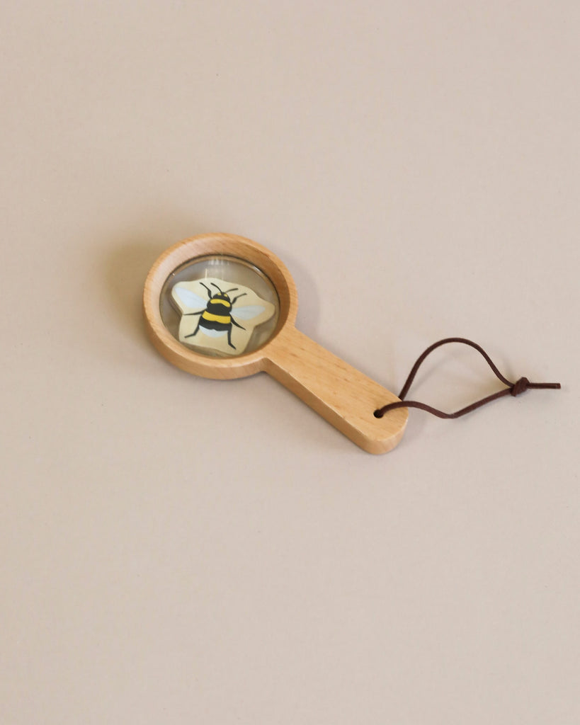 A wooden magnifying glass lying on a plain background, with the lens focusing on a small, detailed illustration of a bee.