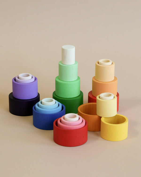 Colorful sustainable wooden Grapat Nesting Bowls arranged in pyramids on a beige background, showcasing a gradient of sizes and hues including blue, green, red, and yellow.