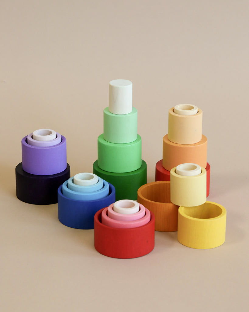 Colorful sustainable wooden Grapat Nesting Bowls arranged in pyramids on a beige background, showcasing a gradient of sizes and hues including blue, green, red, and yellow.