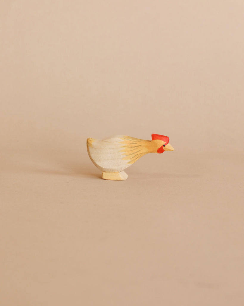 A small, hand-carved Ostheimer Long Neck Hen - Ochre figurine with a natural wood finish and painted red details on a plain beige background, perfect for imaginative play.