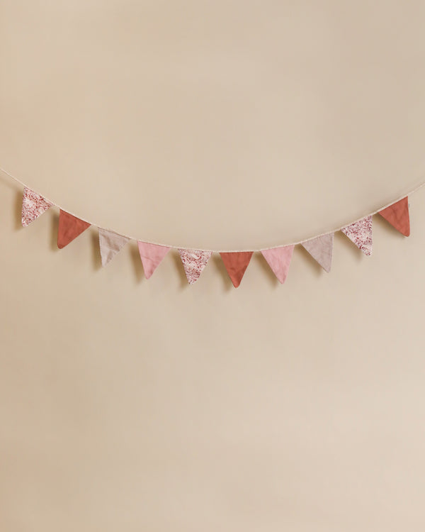 A Maileg garland in shades of pink and patterned gray, hung against a soft beige background.