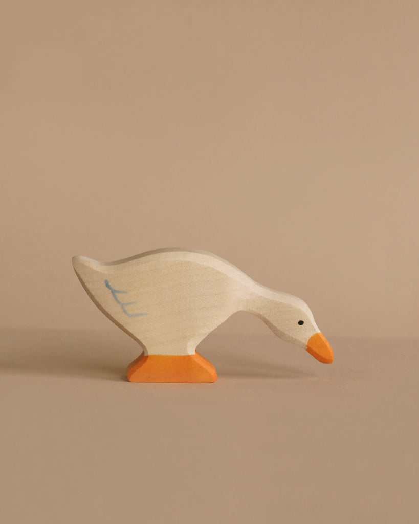 A Holztiger Goose, Feeding painted white with an orange beak and webbed feet is depicted against a plain beige background. The handcrafted wood toy, akin to HOLZTIGER figures, shows the goose in a bending position as if pecking at the ground.