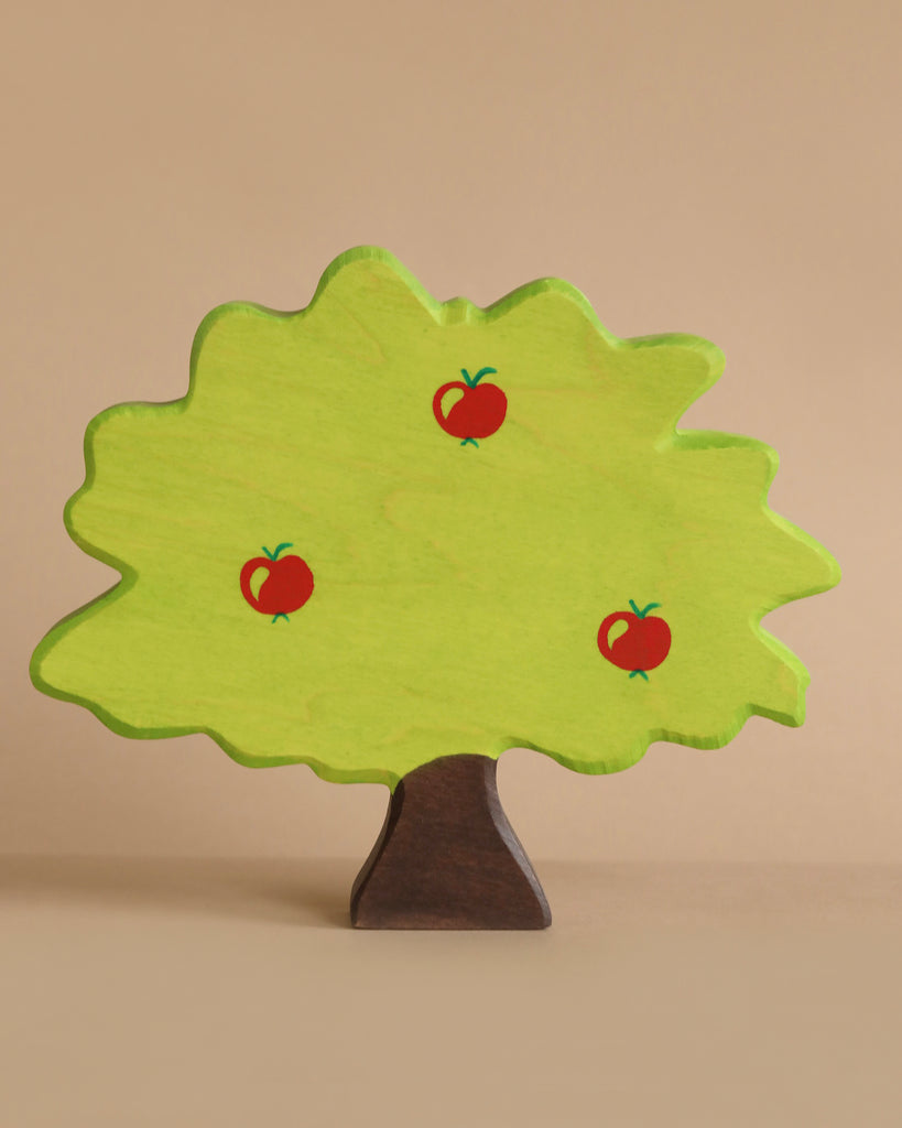 A handcrafted wooden toy tree, made from maple and beech wood, features a light green canopy with a brown trunk and three small red apples. The charming Holztiger Apple Tree is set against a plain beige background.