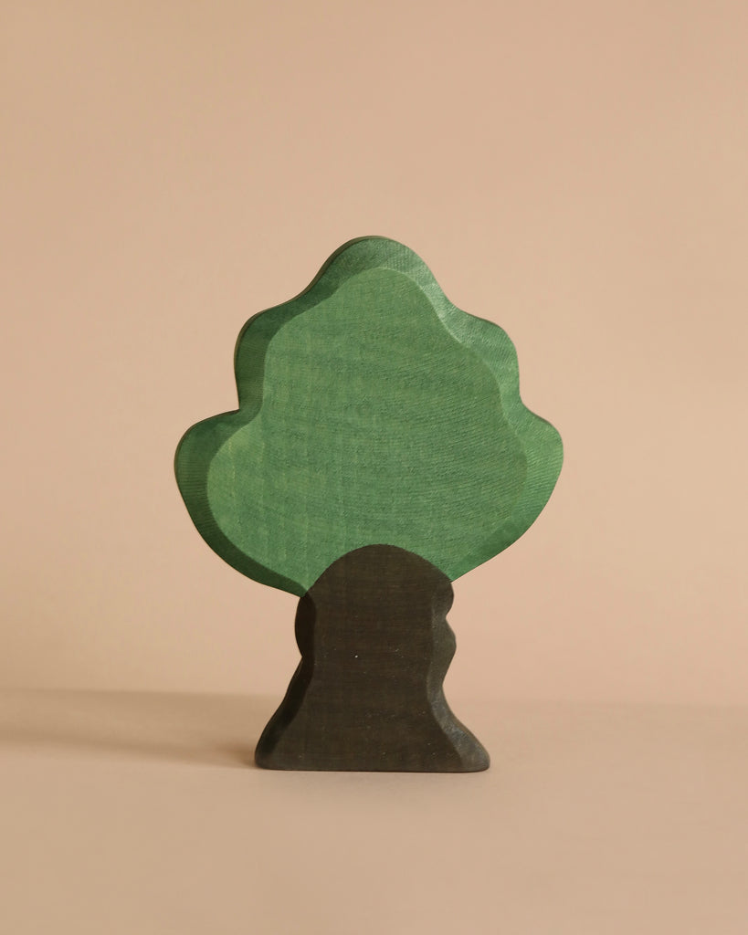 A minimalist wooden tree figurine with a green treetop and a brown trunk stands against a beige background. The softly rounded edges evoke a natural aesthetic, perfect for imaginative play often found in handcrafted Ostheimer Oak Tree toys.