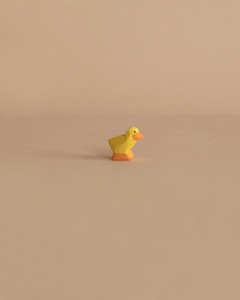 A small, yellow Ostheimer Chick with an orange beak is placed in the center of a beige background, creating a minimalistic composition that invites imaginative play.