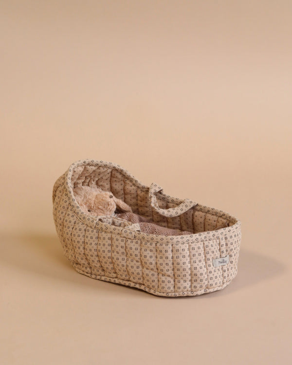 A Maileg Carry Cot, Large - Sand, with a charming floral pattern sits on a neutral background, resembling a quaint portable bed. It holds a soft, fuzzy brown teddy bear.