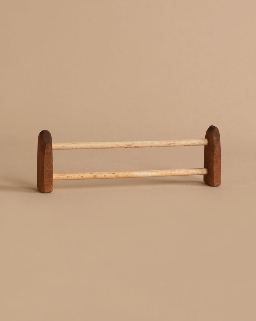 A minimalist wooden towel rack with two parallel rods and ends made of darker wood. The design echoes the handcrafted charm of the Ostheimer Fence, Small, set against a sandy beige background to create a cohesive and subtle aesthetic perfect for imaginative play in any space.