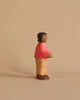 A small, handcrafted wooden figurine of a person stands against a beige background. The figure, dressed in a red sweater, tan pants, and brown shoes, has a simple, minimalist design with a smooth texture and neutral facial expression. Made using sustainably sourced materials, it evokes the charm of an Ostheimer Son, Red Sweater.