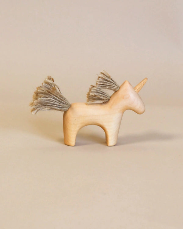 A **Handmade Wooden Unicorn** made from maple wood with a simple, minimalist design stands on a neutral background. Coated in natural linseed oil, the unicorn features a single horn and a mane and tail of coarse, light-colored threads. Suitable for children 3 and up.