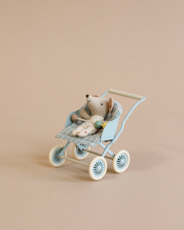 A small, stuffed toy mouse is seated in a Maileg Stroller, Baby Mice - Mint. The mouse, part of the tiny mouse families, is tucked in with a checkered blanket. The stroller, perfect to transport babies or toys alike, is set against a plain beige background.