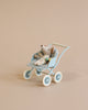 A small, stuffed toy mouse is seated in a Maileg Stroller, Baby Mice - Mint. The mouse, part of the tiny mouse families, is tucked in with a checkered blanket. The stroller, perfect to transport babies or toys alike, is set against a plain beige background.