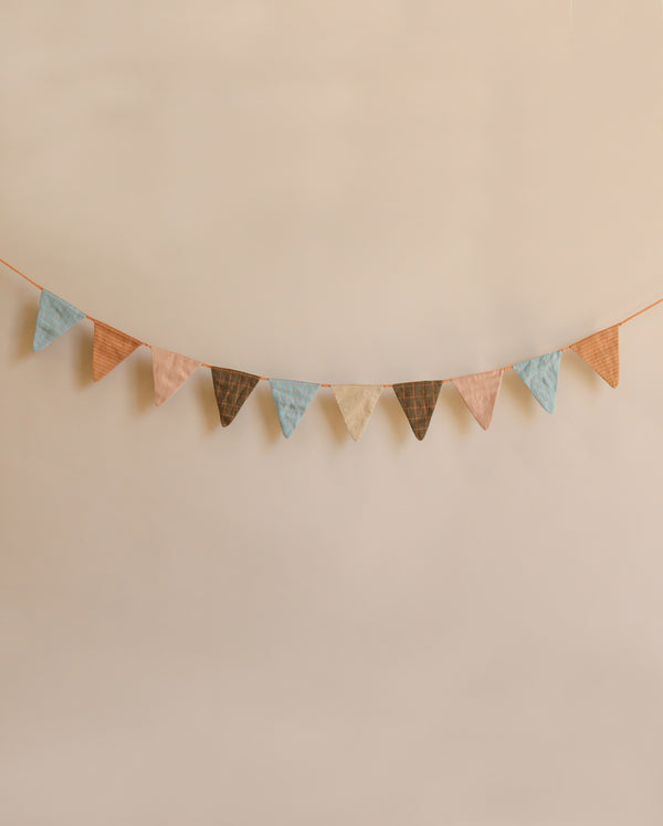 A string of Maileg Garland - Ocher flags in festive multi-colored shades of pink, blue, and brown hangs against a soft beige background.