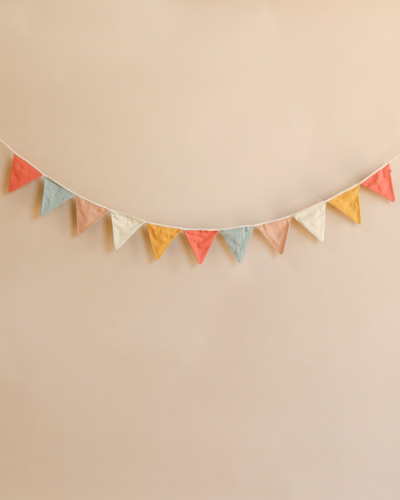 A festive garland of pastel-colored triangular flags hangs against a neutral background. The multi-colored fabrics in pink, blue, yellow, and white are evenly spaced and connected by a single string, creating a cheerful decoration perfect for playrooms and nurseries. The Maileg Garland - Multi is an ideal choice for adding charm to any space.