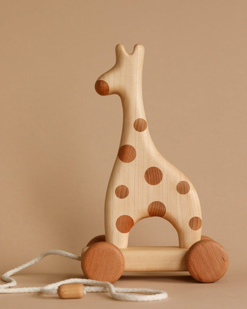 A **Handmade Wooden Giraffe Pull Toy** shaped like a giraffe with brown circular spots stands against a beige background. This delightful kids toy with wheels features four wooden wheels and a white pull string attached to a small wooden handle.