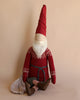 A Maileg Large Santa (Size: 45.27 in.) with a long white beard and a tall red hat is seated against a beige background. The Christmas figurine is wearing a lambswool sweater with white patterns, grey pants, and striped socks. A cloth is draped next to the doll.