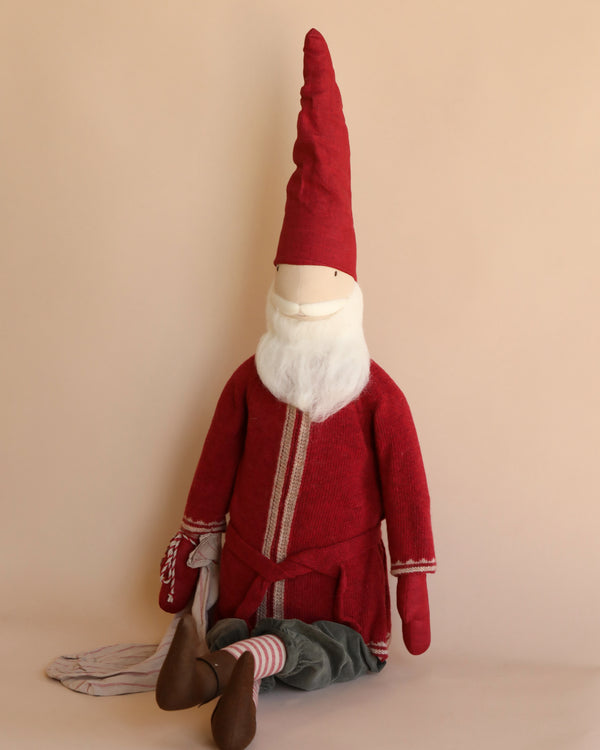 The Maileg Large Santa, standing at 43.30 inches, features a whimsical design with a tall red hat and matching outfit against a plain beige background. Sporting a white beard, light brown shoes, and striped socks, it makes for a charming holiday decoration reminiscent of a plush gnome doll.