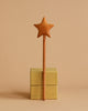 A Handmade Wooden Star Magic Wand crafted from cherry wood with a star-shaped tip is standing upright on top of two stacked yellow gift boxes against a plain beige background.