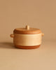 A small, round wooden container with a lid and two side handles. The Handmade Wooden Pretend Pot has a smooth finish and appears to be crafted from light-colored hardwoods like maple or beech. The background is a neutral beige.