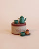 The "Maileg Christmas Set" is a vintage-style tin that includes two teal cups, a matching teapot, and a small bundt cake on a saucer. Please be aware that it contains small parts and may pose a choking hazard for children under three.