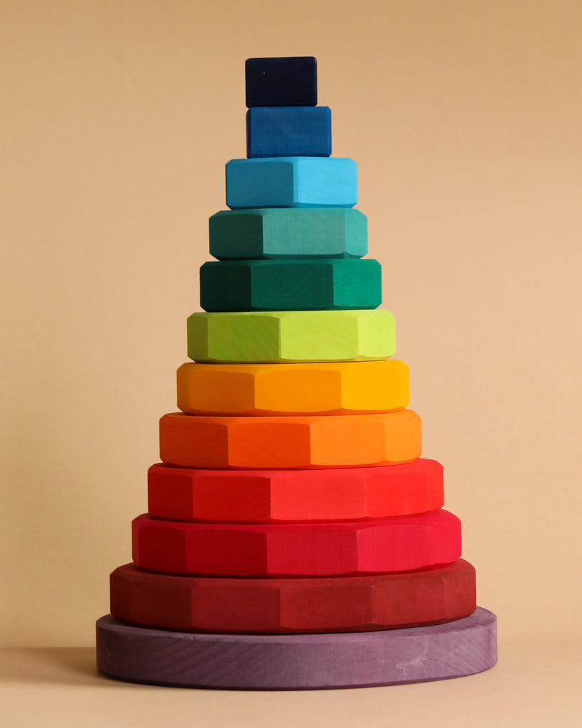 A Grimm's Giant Geometrical Stacking Tower, arranged in gradient colors from dark maroon at the base to dark blue at the top. This fine motor skills toy, fashioned from non-toxic wood, forms a gradually narrowing pyramid against a plain beige background.