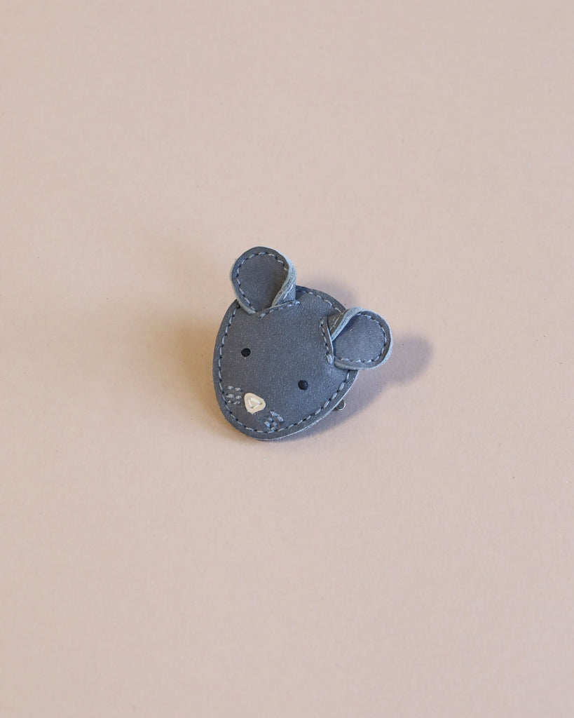 A small gray mouse Donsje Leather Hairclip with intricate stitching and sparkling details, set against a soft pink background, is handmade with premium leather.