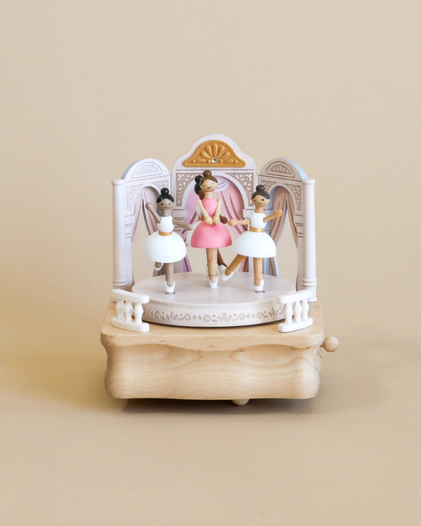 The wooden ballerina music box features a theatrical stage setting, adorned with delicate details. At the center stands a ballerina dressed in a pink dress, and surrounding her are three more ballerinas, each in a graceful stance, wearing white dresses. The ballerinas' features are lovingly painted, showcasing a range of skin tones, adding diversity and depth to the scene.