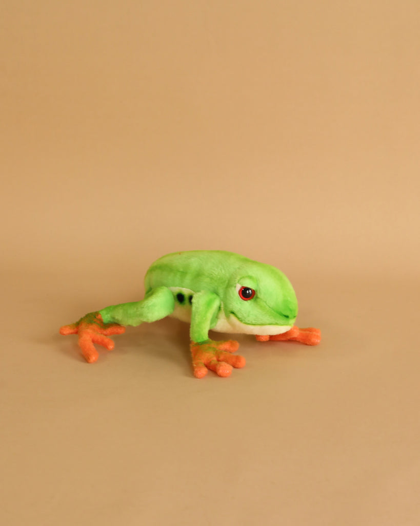 A hand-sewn Tree Frog Stuffed Animal, resembling a green frog with orange feet and hands, on a smooth beige background.