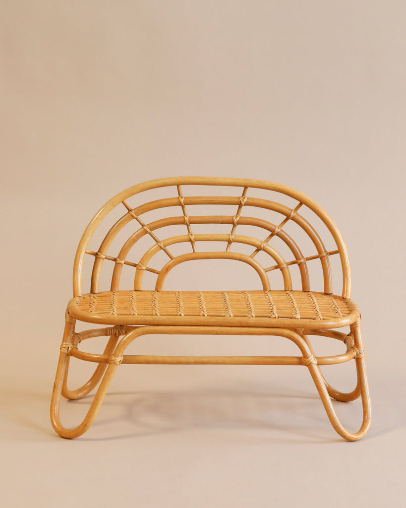 The Kid’s Rattan Bench features an intricate, curved backrest and a woven seat with a natural wood finish. The bench boasts a minimalist design, standing on four looping legs that blend traditional and contemporary styles harmoniously. As part of the basket furniture series, it complements neutral beige backgrounds perfectly.