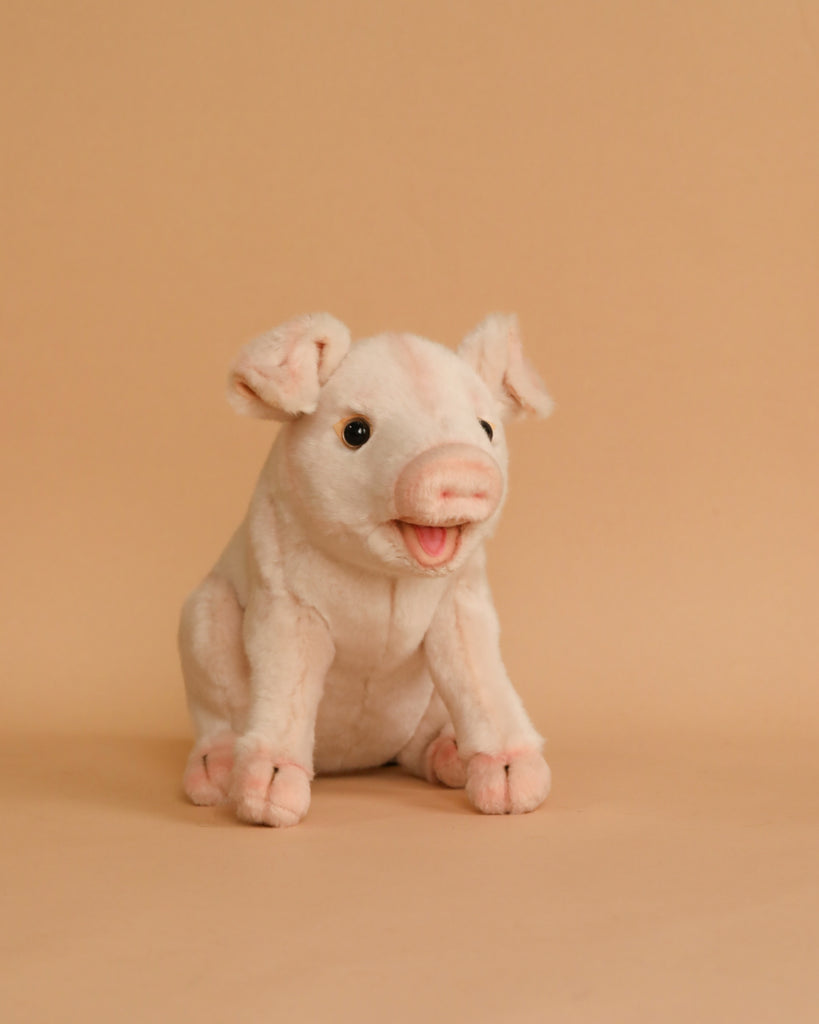 A cute Pig Stuffed Animal with a friendly expression, standing upright on a beige background. The toy is light pink with darker pink inside its floppy ears and a small, open-mouthed smile.